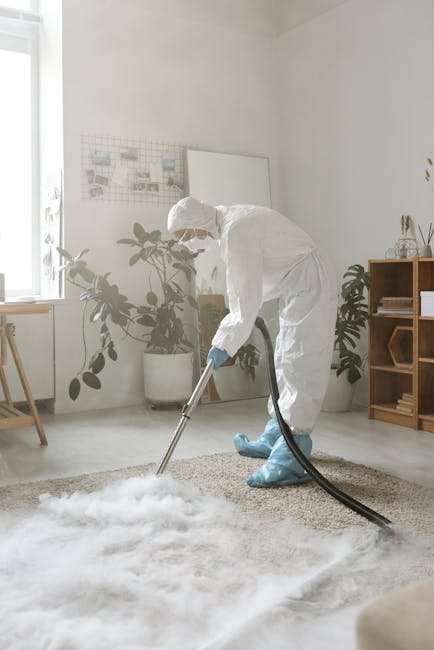 A woman vacuuming a patterned, beige and green area rug in a living room with wooden flooring and a brown leather sofa. She is using a yellow and black handheld vacuum cleaner, dressed in casual cloth