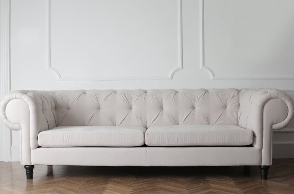 A long, bright blue upholstered bench with cushioned seats and backrests, positioned against a plain white wall in a well-lit indoor space. The bench is clean and free of clutter, with a smooth, shiny